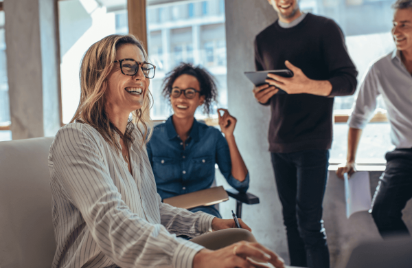 Femme blonde à lunette qui souris entourée de ses collègues de travail