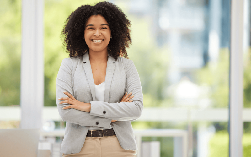 Femme métisse souriante et debout les bras croisés.